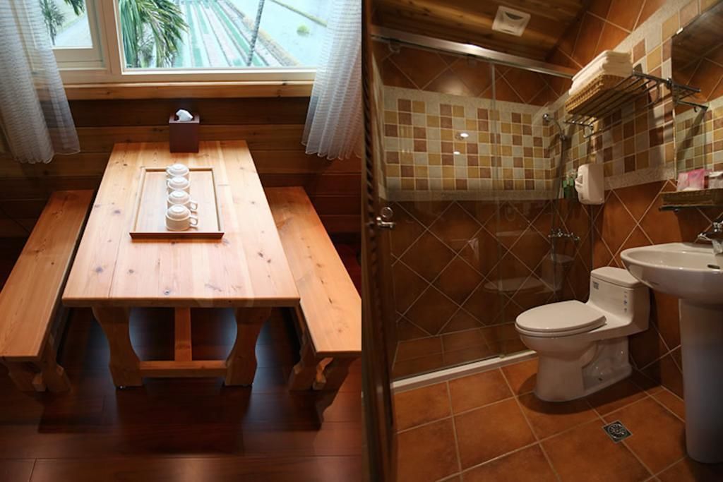 A wooden table with a tray of cups and a tissue box, a shower area with a glass door, and a toilet with a sink.