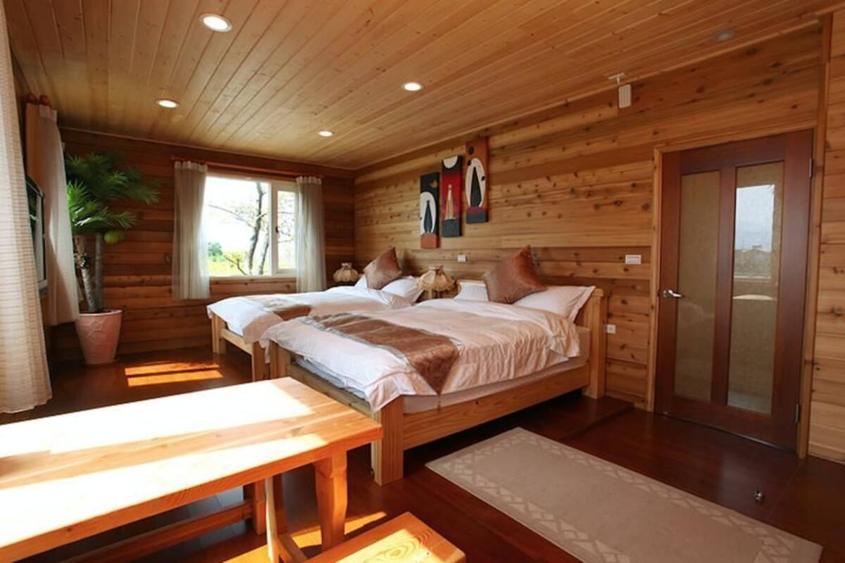 A wooden cabin bedroom with two beds, a bench, and a door.