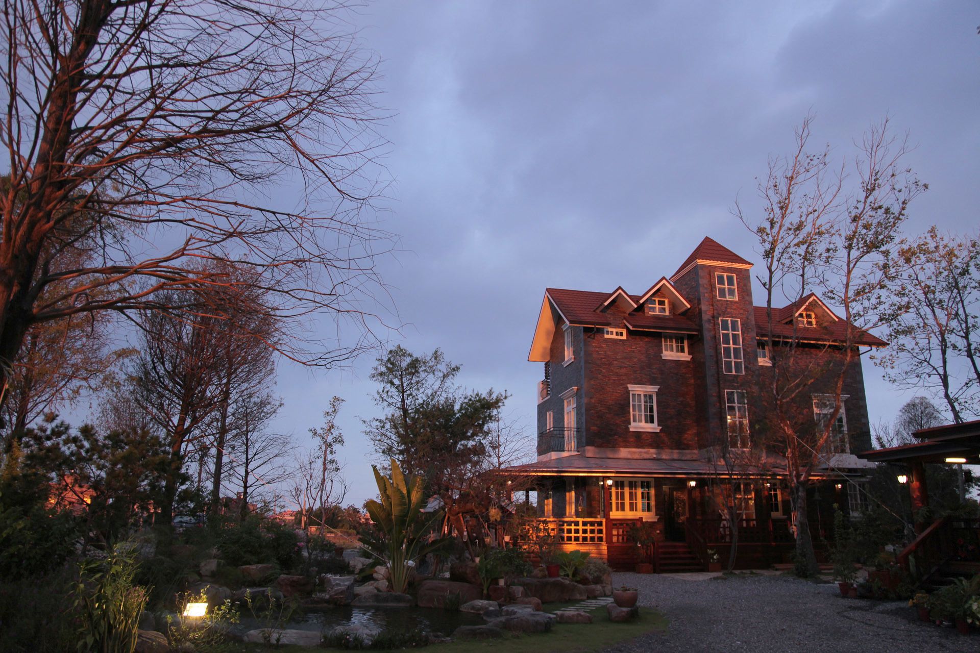 Uma casa grande, com vários andares, um alpendre destacado e um jardim bem cuidado.