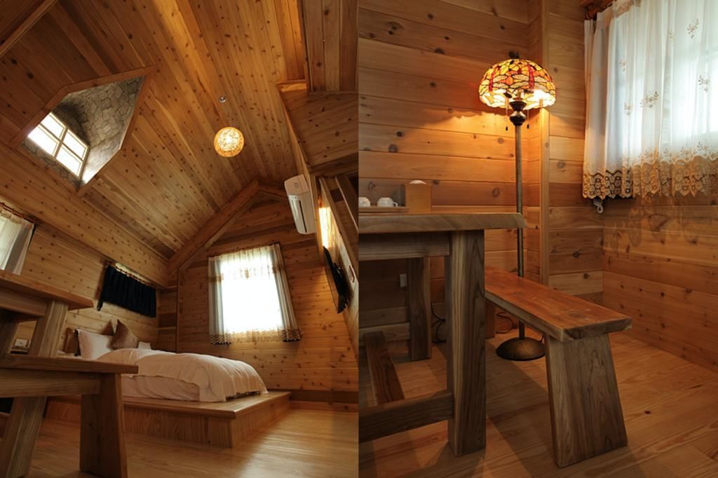 A cozy wooden cabin room with a bed, a bench, a table, and a stained glass lamp.