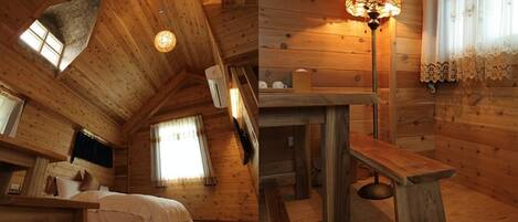 A cozy wooden cabin room with a bed, a bench, a table, and a stained glass lamp.
