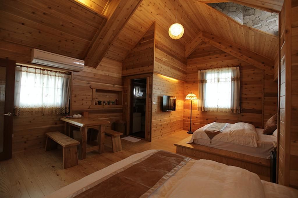 A cozy log cabin room with a wooden interior, a bed, a desk, and a television.