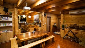Interior de uma cabana de madeira com mesa, banco, estante e uma bicicleta.