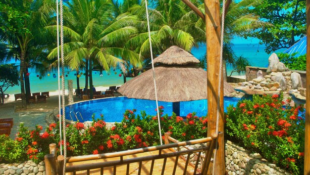 Un resort tropical con piscina, palmeras y una cabaña con techo de paja.