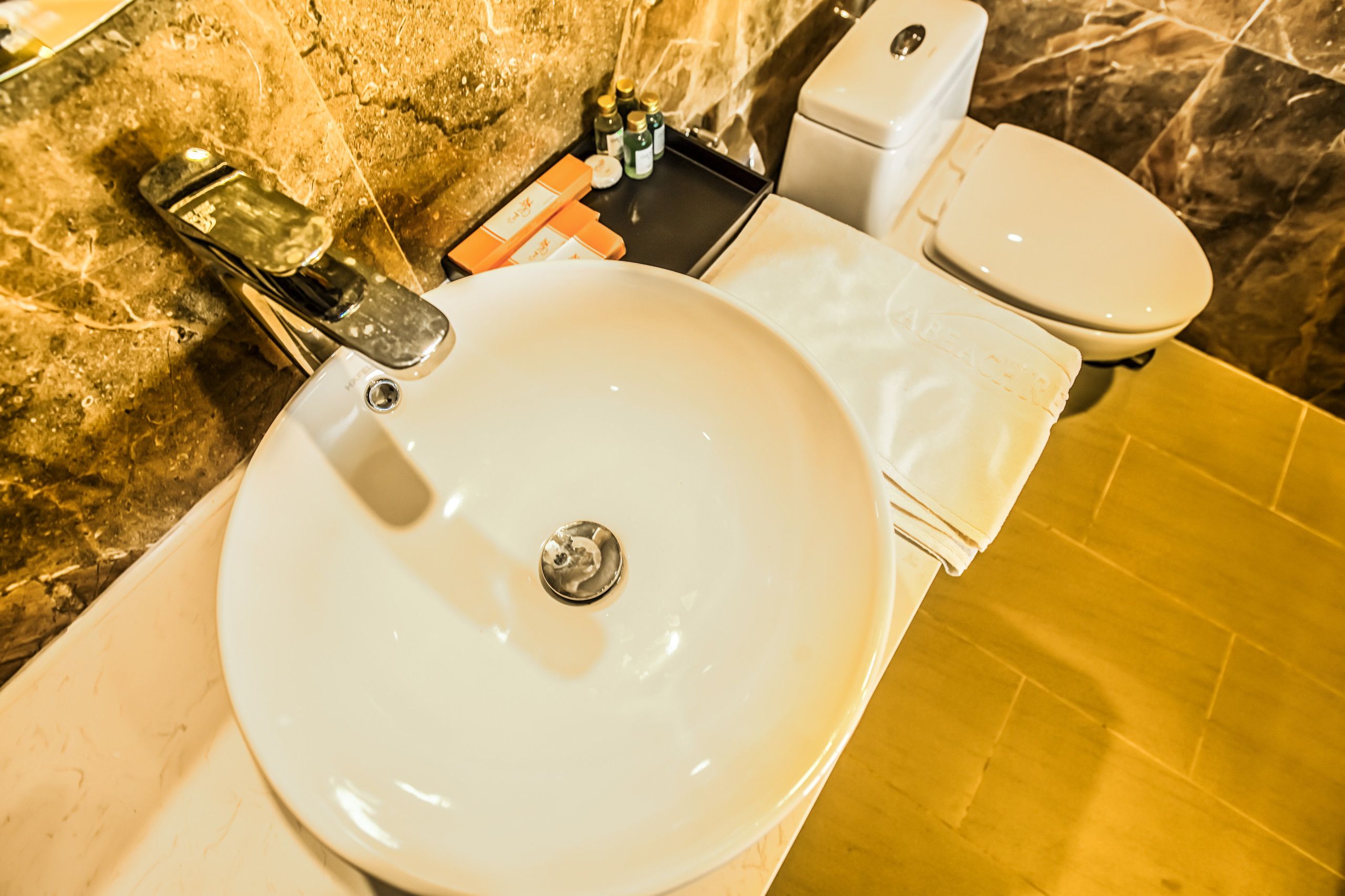 A bathroom with a white sink, a toilet, and a marble wall.