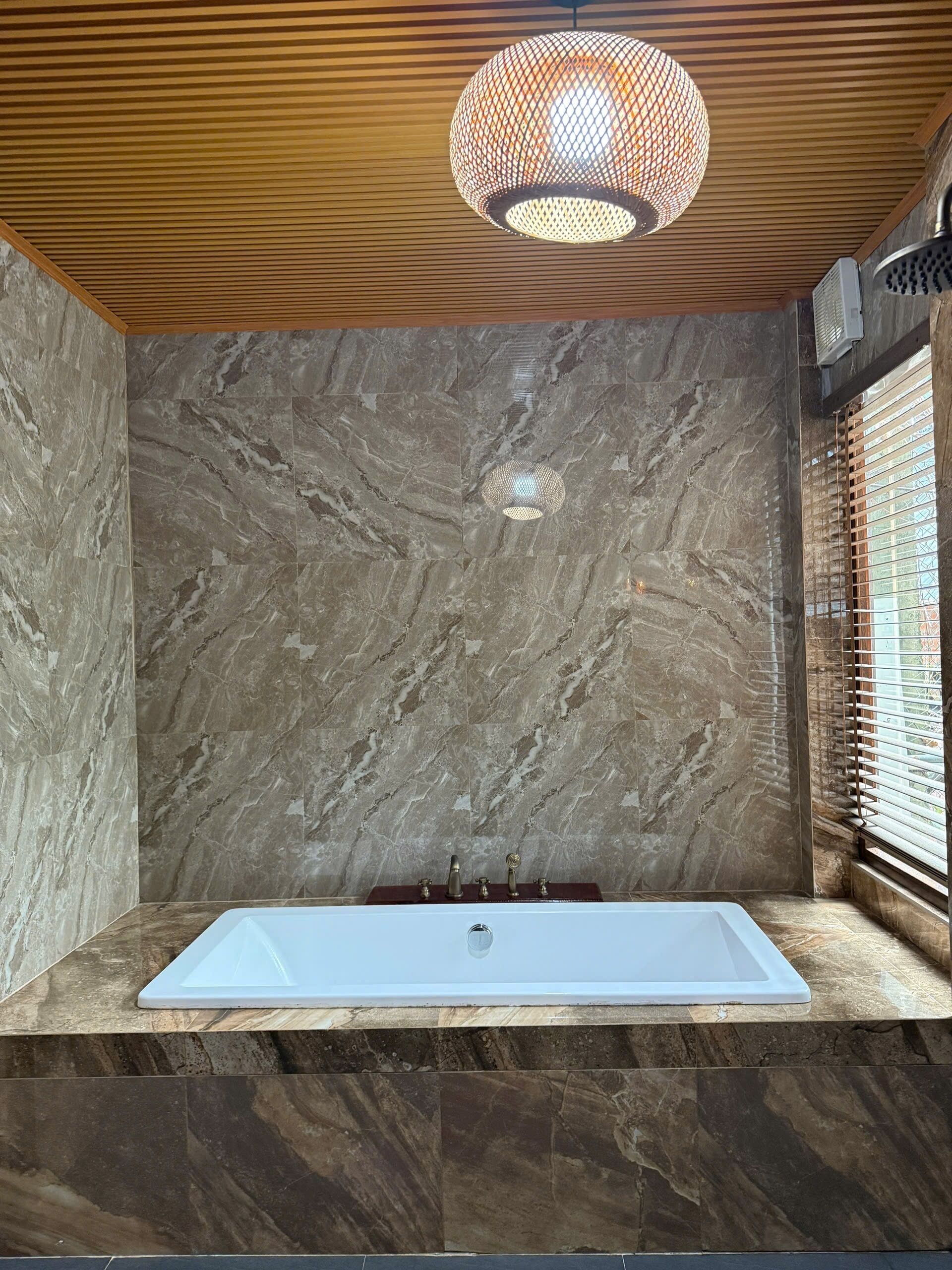 A modern bathroom with a marble wall, a freestanding bathtub, and a unique ceiling light fixture.