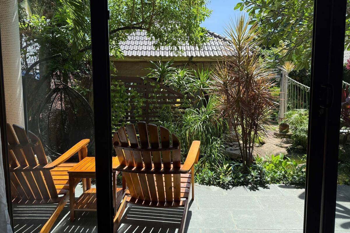 Ein Terrassenbereich mit Holzkohlen, einem Tisch, umgeben von üppiger Bepflanzung und einer Dachkonstruktion mit Ziegeln.