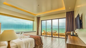 Habitación de hotel con cama, escritorio, silla, televisor y balcón con vista al mar.