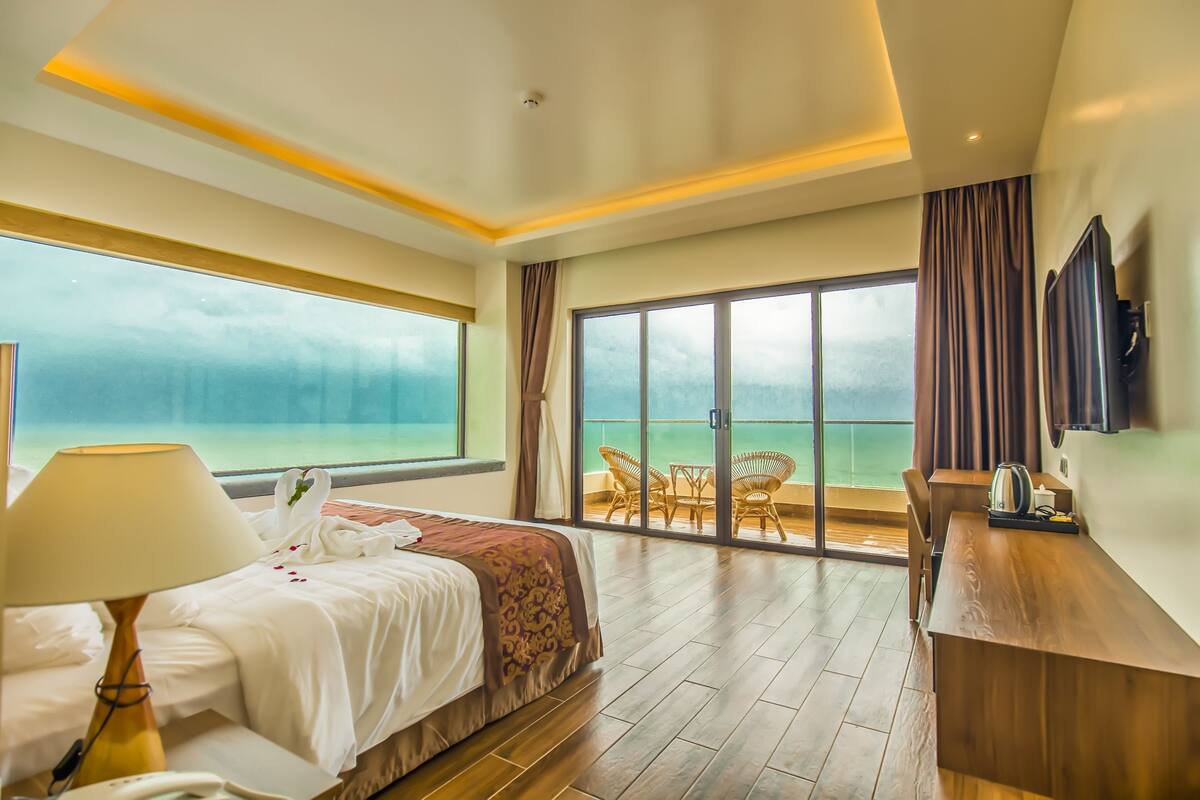 Ein Hotelzimmer mit Bett, Schreibtisch, Stuhl, Fernseher und einem Balkon mit Meerblick.