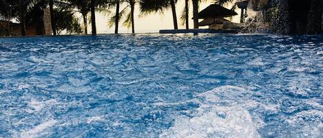 A pool with clear water, surrounded by palm trees and a rock structure.