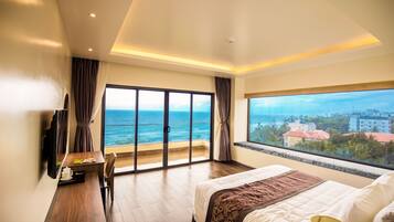 Habitación de hotel con una cama grande, un escritorio, un televisor y vistas al océano.