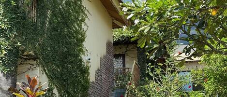 A building with a staircase leading to a balcony, surrounded by greenery and a rope barrier.