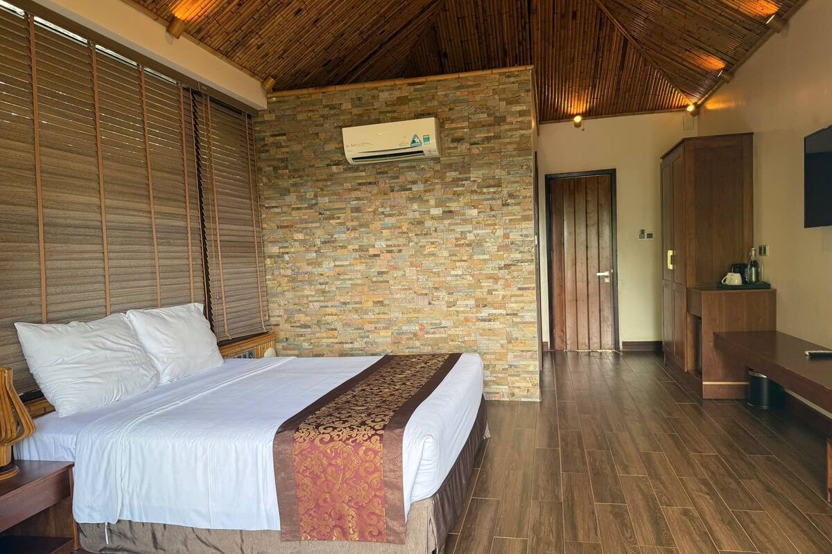 Ein Schlafzimmer mit einem großen Bett, Holzboden, einer Steinwand und einer Holzbalkendecke.