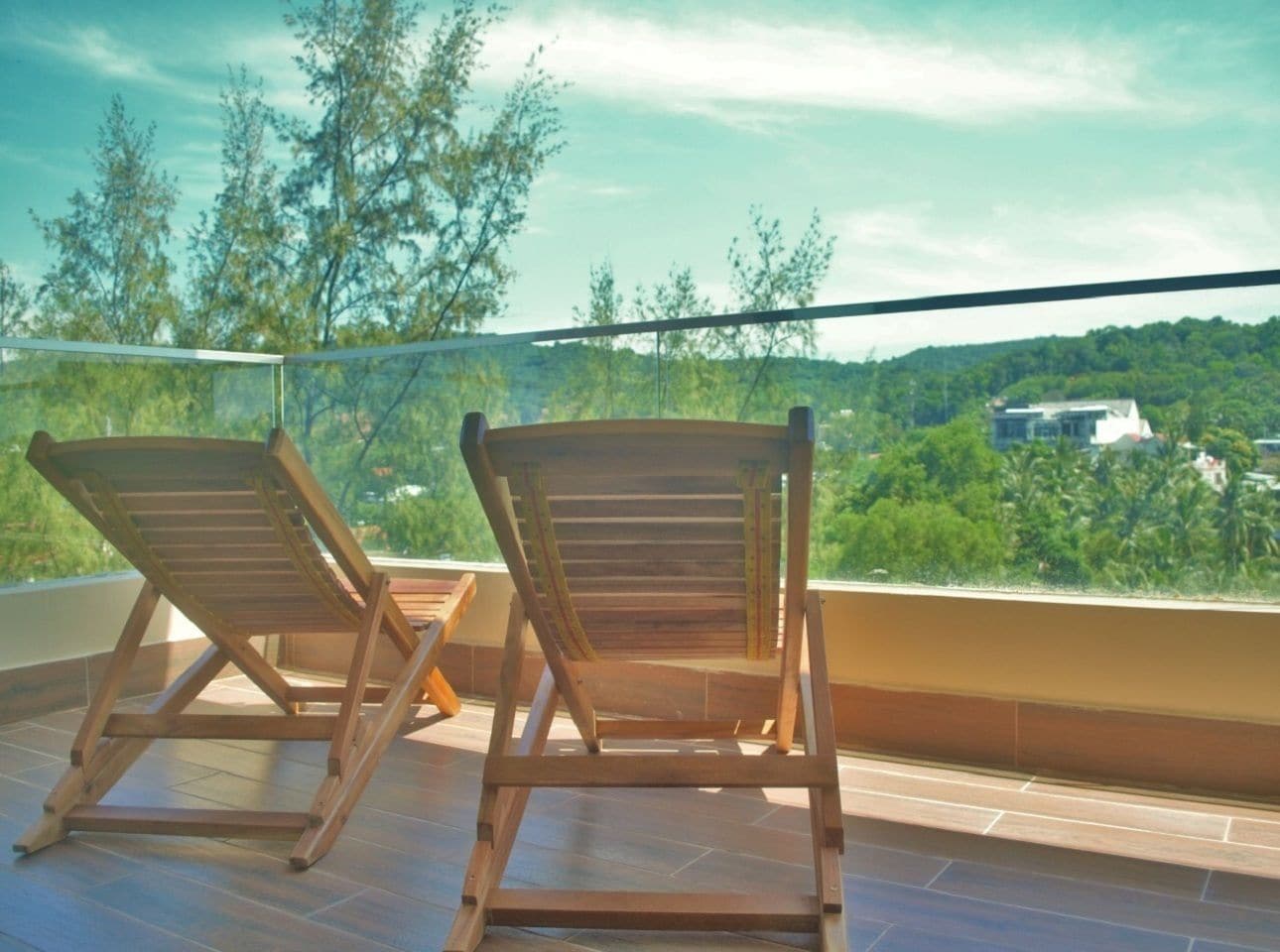 Due poltrone in legno su un balcone con vista su un paesaggio verde e edifici in lontananza.