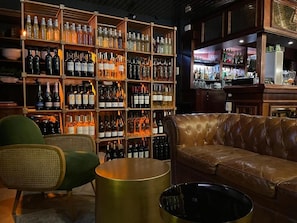 Un espace bar avec des étagères remplies de bouteilles, un canapé en cuir et une table ronde.