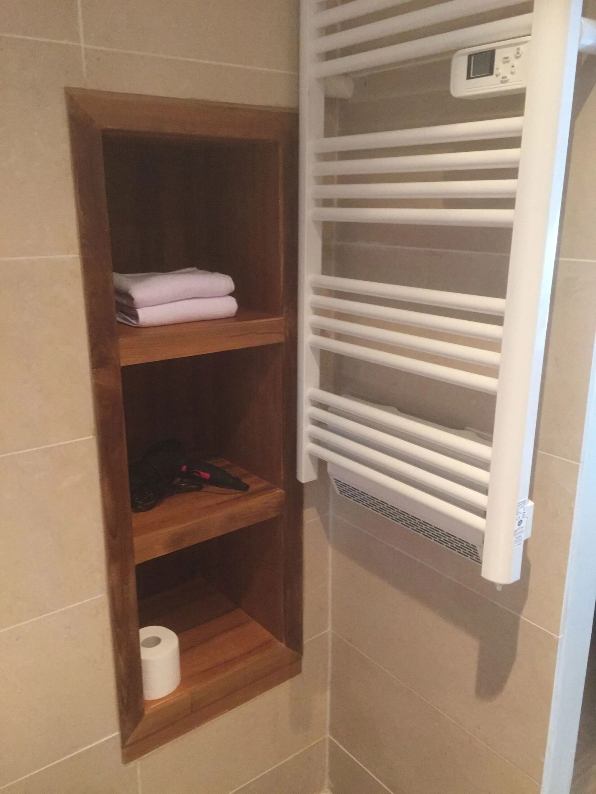 A bathroom with a wooden shelf unit containing towels and a toilet paper roll.