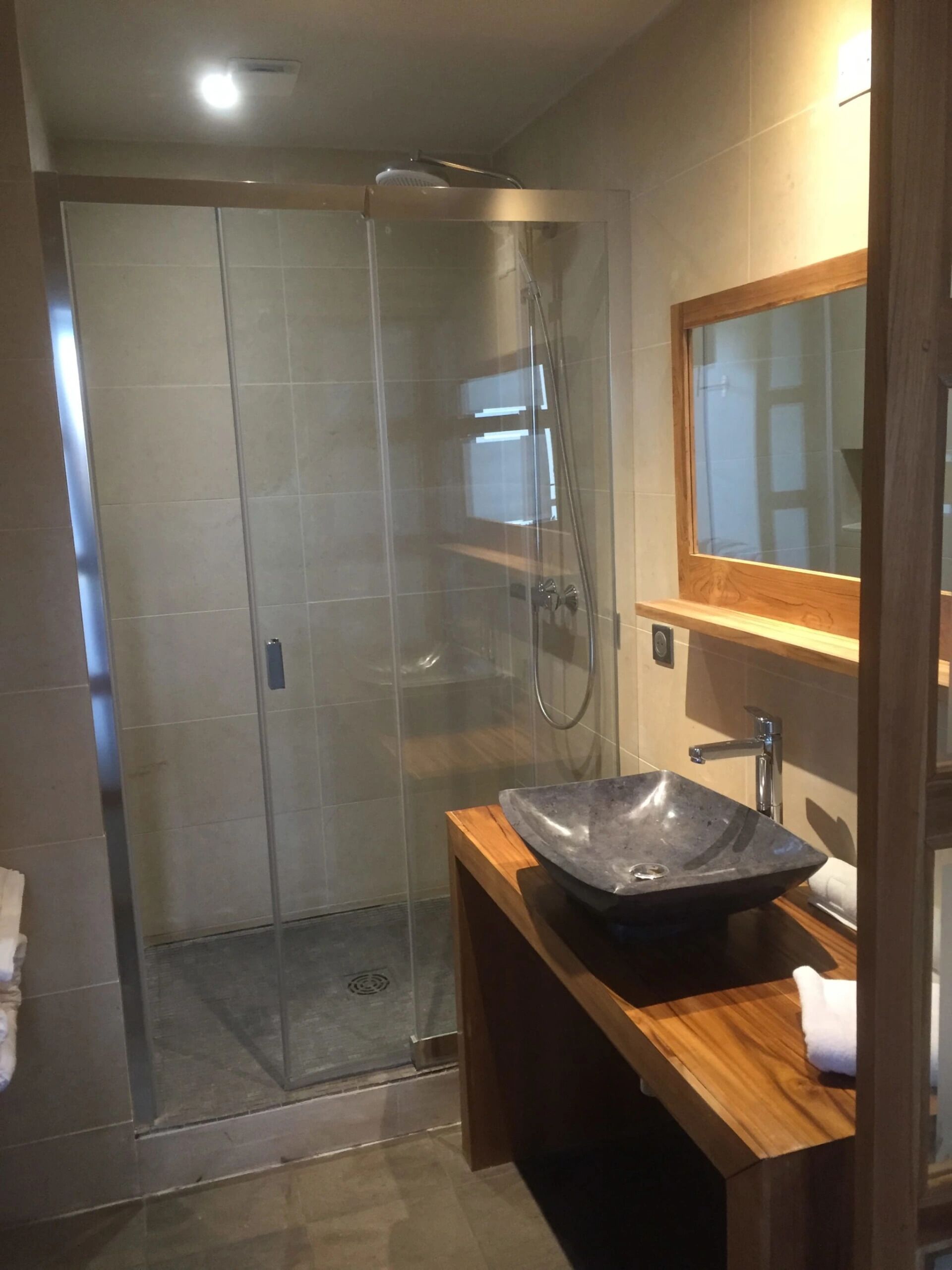 A modern bathroom with a glass-enclosed shower, a wooden vanity with a large vessel sink, and a mirror above the sink.