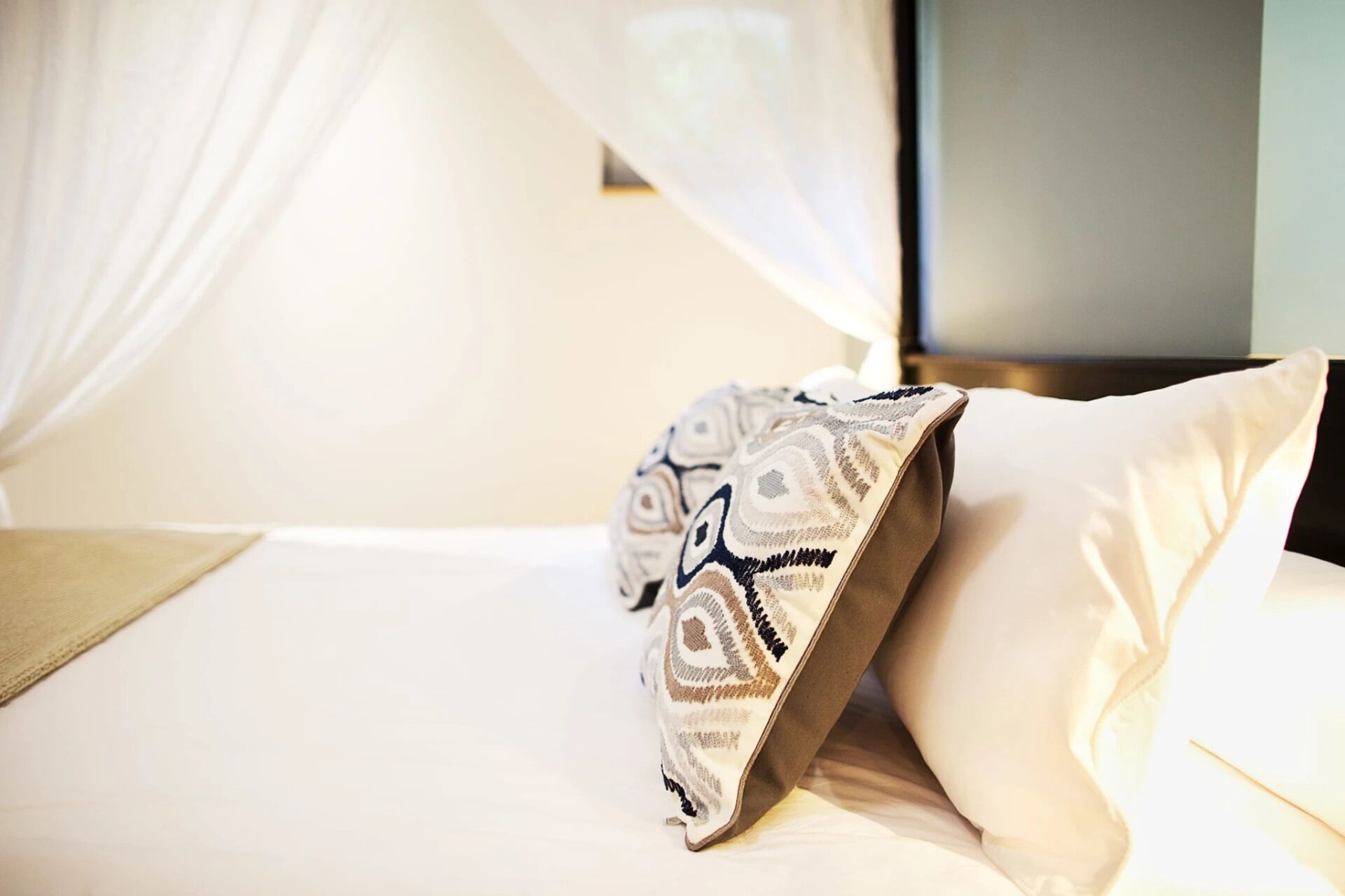 Ein Bett mit einem gemusterten Kissen und einem transparenten Vorhang.