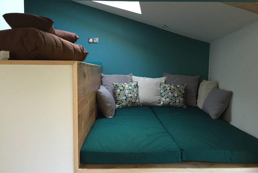 A cozy room with a green sofa bed, a wooden headboard, and a skylight.