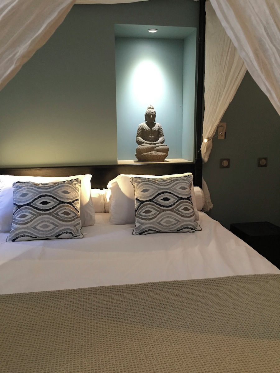 A bed with a canopy, a Buddha statue, and patterned pillows.