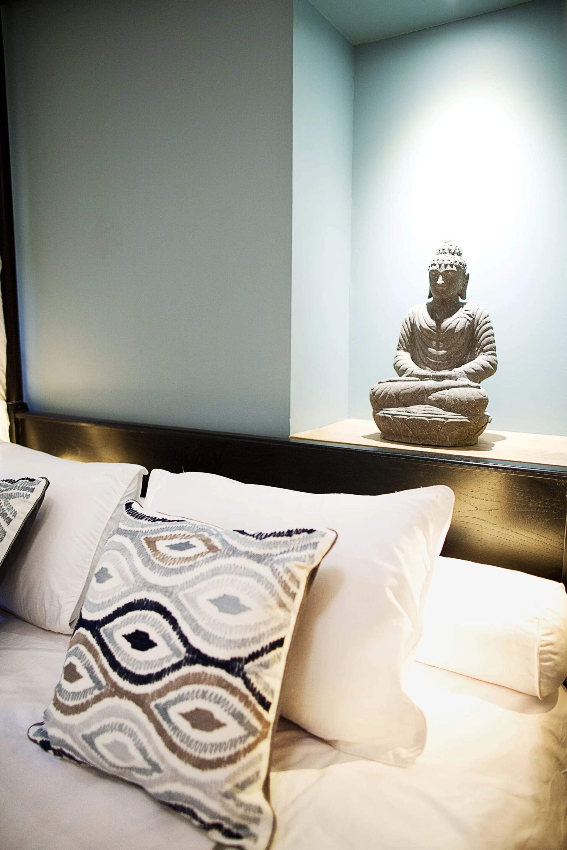 Una cama con almohadas estampadas y una estatua de una figura meditando sobre una repisa.