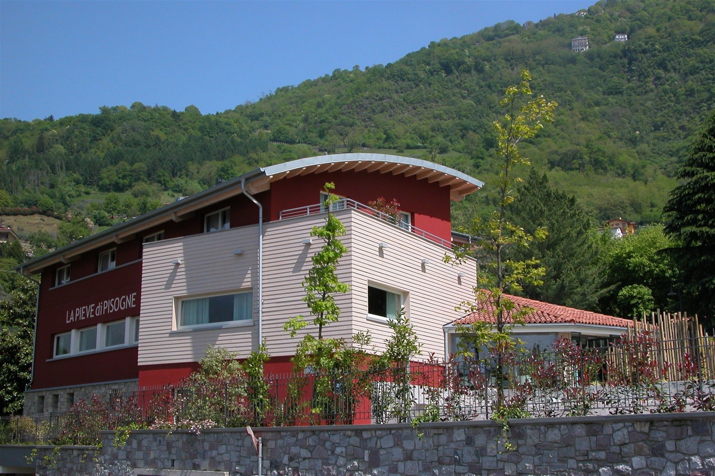 Un edificio de dos pisos con fachada roja y blanca, un balcón y un muro de piedra en frente.
