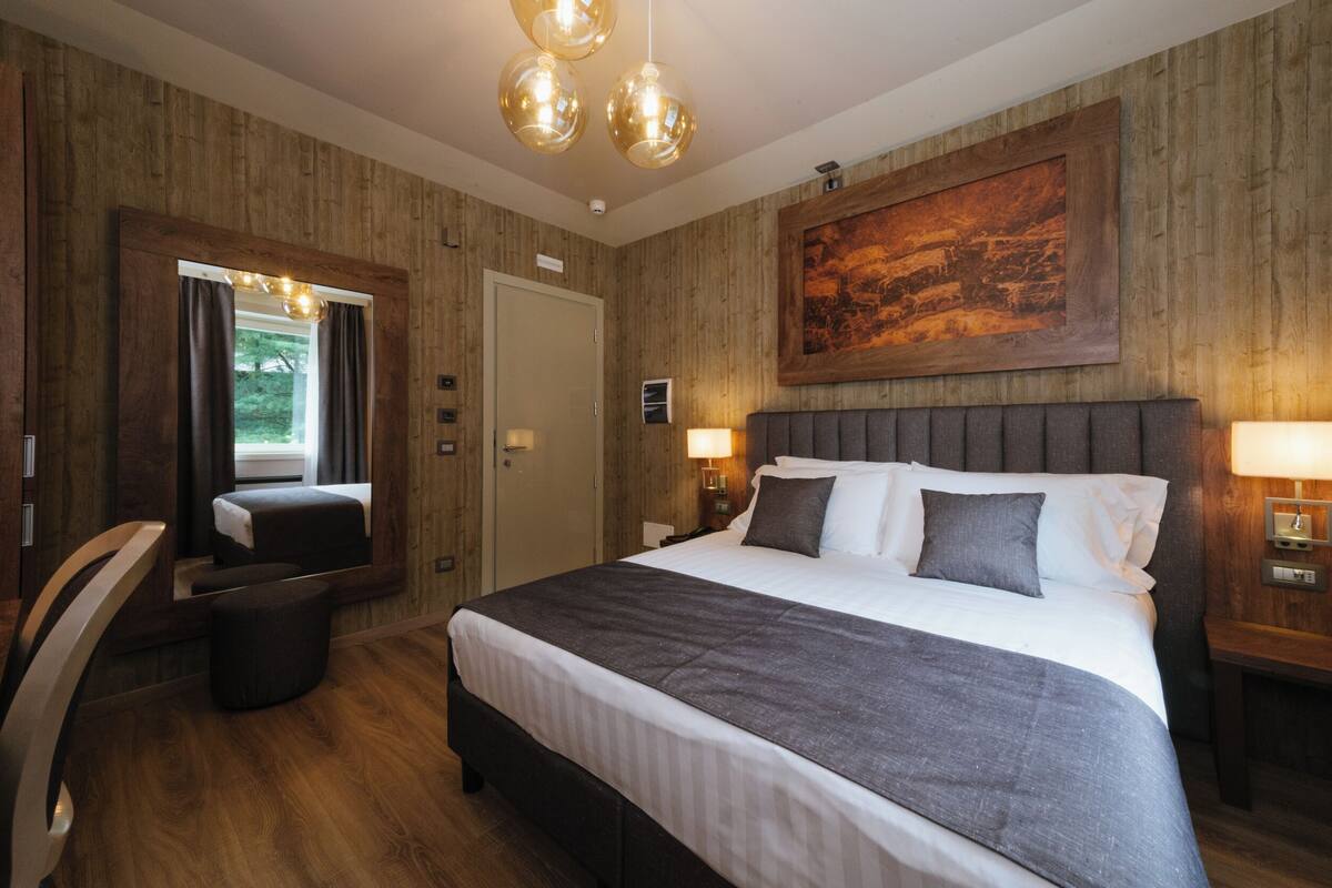 A hotel room with a large bed, a mirror, a wooden wall, and a painting.
