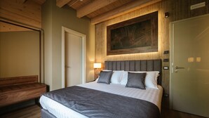A bedroom with a large bed, a wooden bench, a door, and a wall-mounted artwork. - Lake Hotel La Pieve (Pisogne)