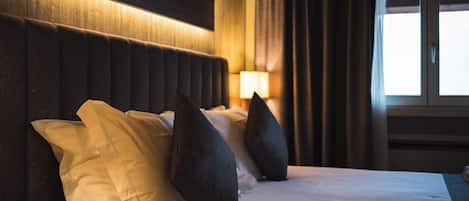 Una habitación de hotel con una cama grande, cabecera oscura y una ventana con cortinas.