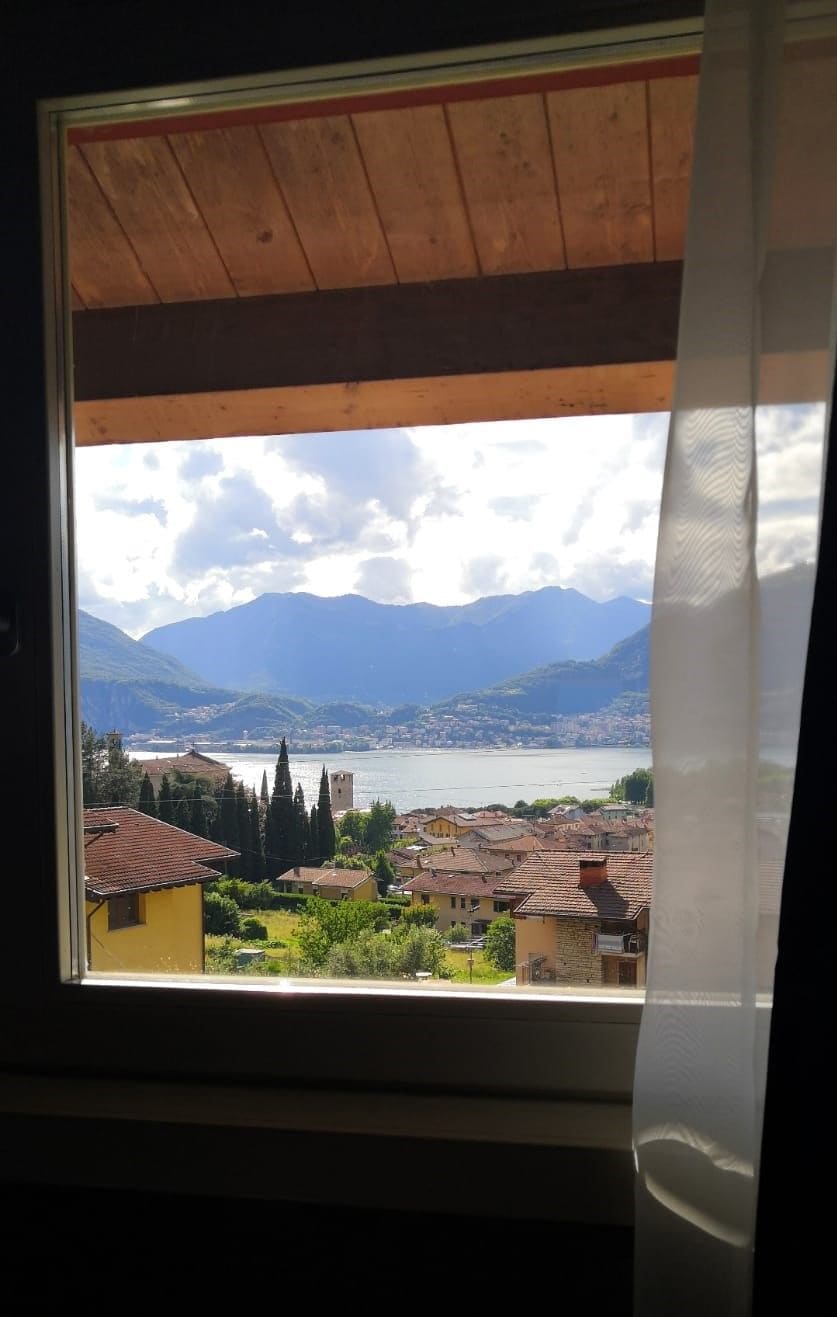 Vista desde una ventana: un lago con montañas al fondo, un pueblo debajo y un techo de madera.
