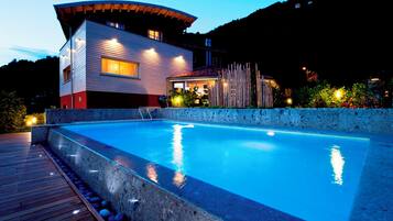 A modern house with a swimming pool, wooden deck, and a mountain backdrop.