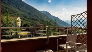 A balcony with a table and chairs, overlooking a mountainous landscape with a building in the background. - Lake Hotel La Pieve (Pisogne)