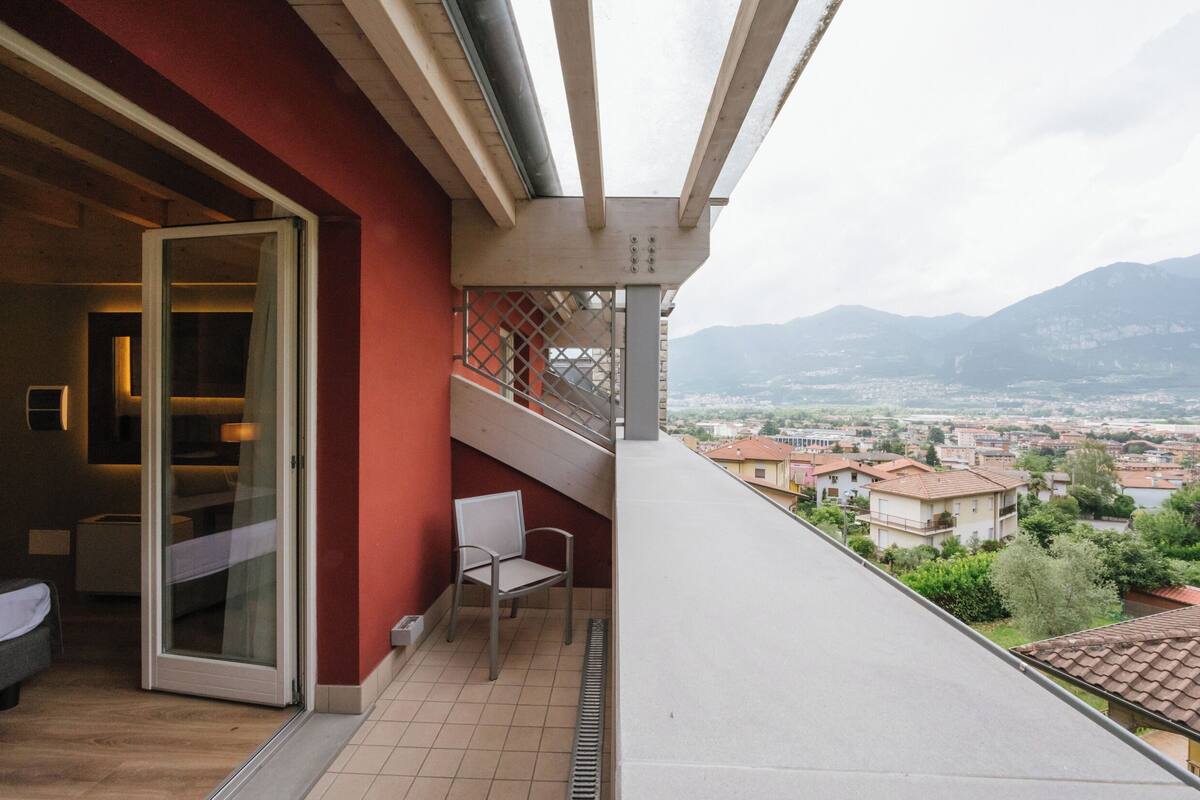 A balcony with a glass door leading to a room, a chair, and a view of a town and mountains.