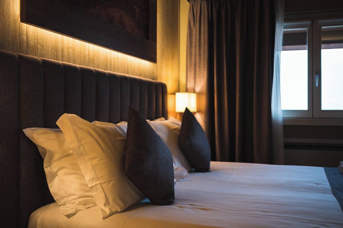 A hotel room with a large bed, dark headboard, and a window with curtains.