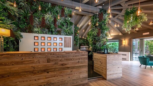 A reception area with wooden reception desk, hanging plants, and a coffee machine. - Lake Hotel La Pieve (Pisogne)