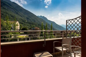 A balcony with a table and chairs, overlooking a mountainous landscape with a building in the background.