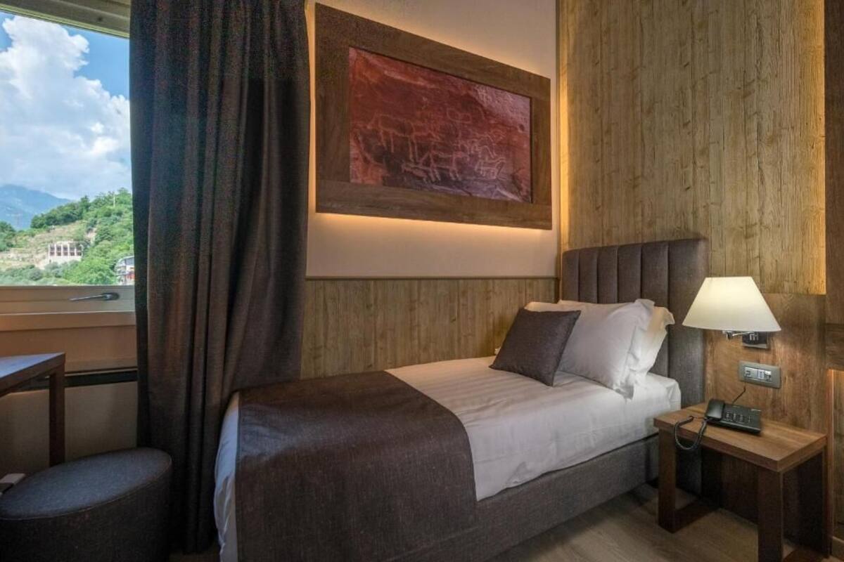 A hotel room with a bed, bedside table, lamp, and a painting on the wall.