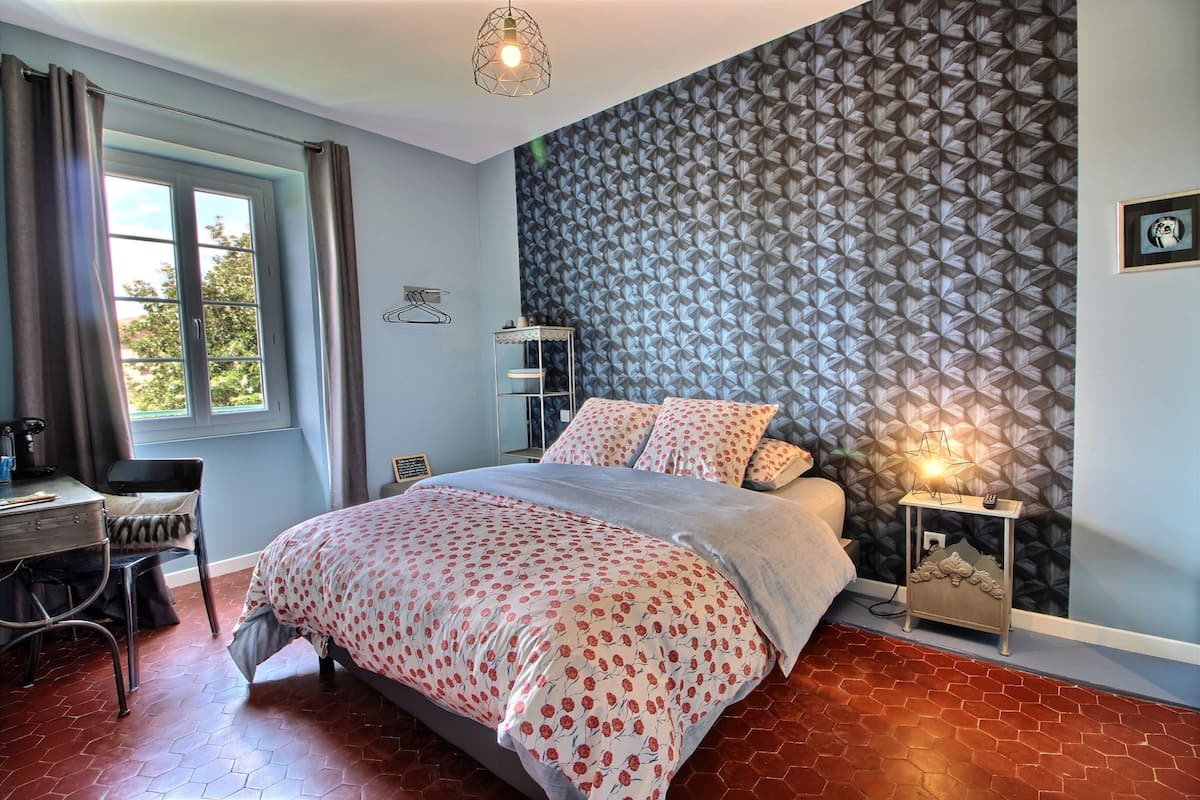 Une chambre à coucher comprenant un lit, un bureau, une chaise, une table de chevet et un mur décoré d’un motif.