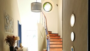 Un pasillo con una consola de madera, una planta en maceta y un adorno con un mapa mundial. Una escalera con barandillas azules conduce a un rellano con un ventanal circular.