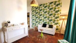 Una sala de estar moderna con un sofá blanco, una cafetera, una lámpara de mimbre y una pared con un diseño de hojas.