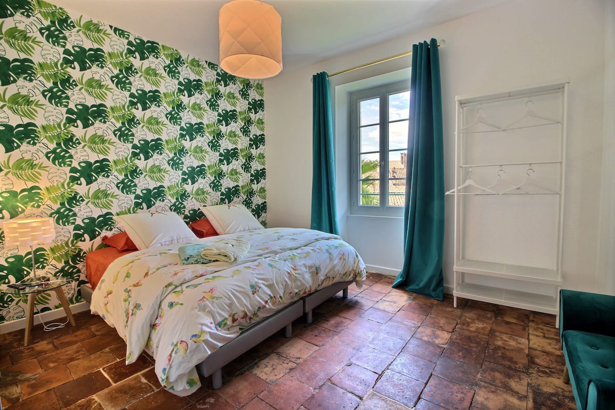 Une chambre à coucher avec un lit, une fenêtre avec des rideaux, un étendoir fixé au mur et un papier peint à motifs.