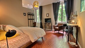 Un dormitorio con cama, escritorio, silla, televisor y ventana con cortinas.