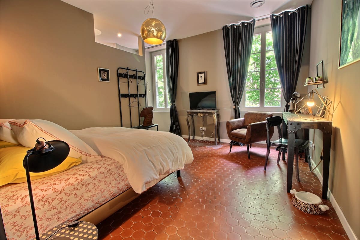 Une chambre à coucher comprenant un lit, un bureau, une chaise, un téléviseur et une fenêtre avec des rideaux.