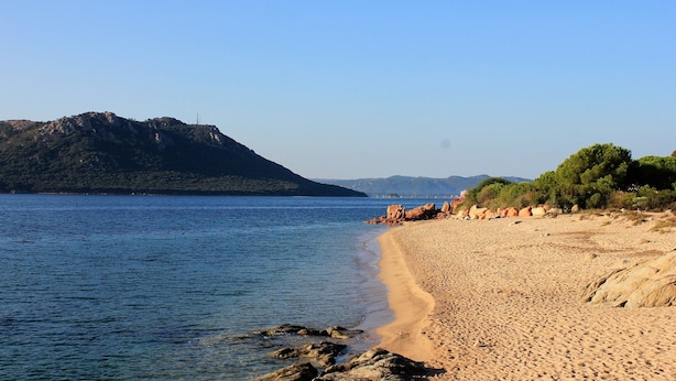 A beach with clear water, rocky outcrops, and a distant mountain. - Résidence Cala Corsa (Lecci)