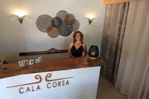 Un comptoir d’accueil avec une enseigne indiquant « CALA CORSA » et une autre, placée au-dessus, sur laquelle on peut lire « Bienvenue ».