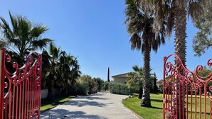 A paved pathway flanked by red wrought iron gates, leading to a building with a tiled roof. - Résidence Cala Corsa (Lecci)