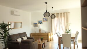 A living room with a sofa, armchair, dining table, chairs, and a potted plant. - Résidence Cala Corsa (Lecci)