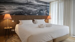 A hotel room with a large bed, two bedside lamps, a large painting on the wall, and a window with curtains. - Hotel Zenite (Angra do Heroismo)