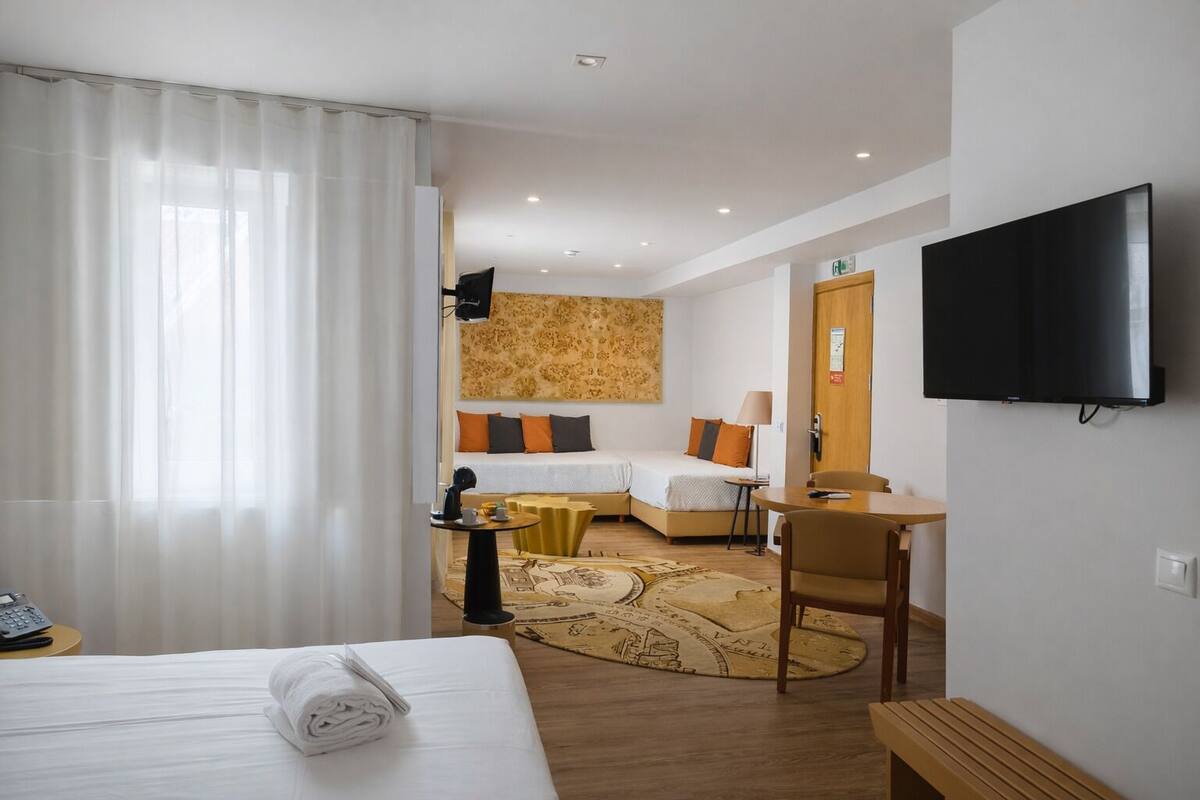 Una habitación de hotel con cama, sofá, escritorio, televisor y alfombra estampada.