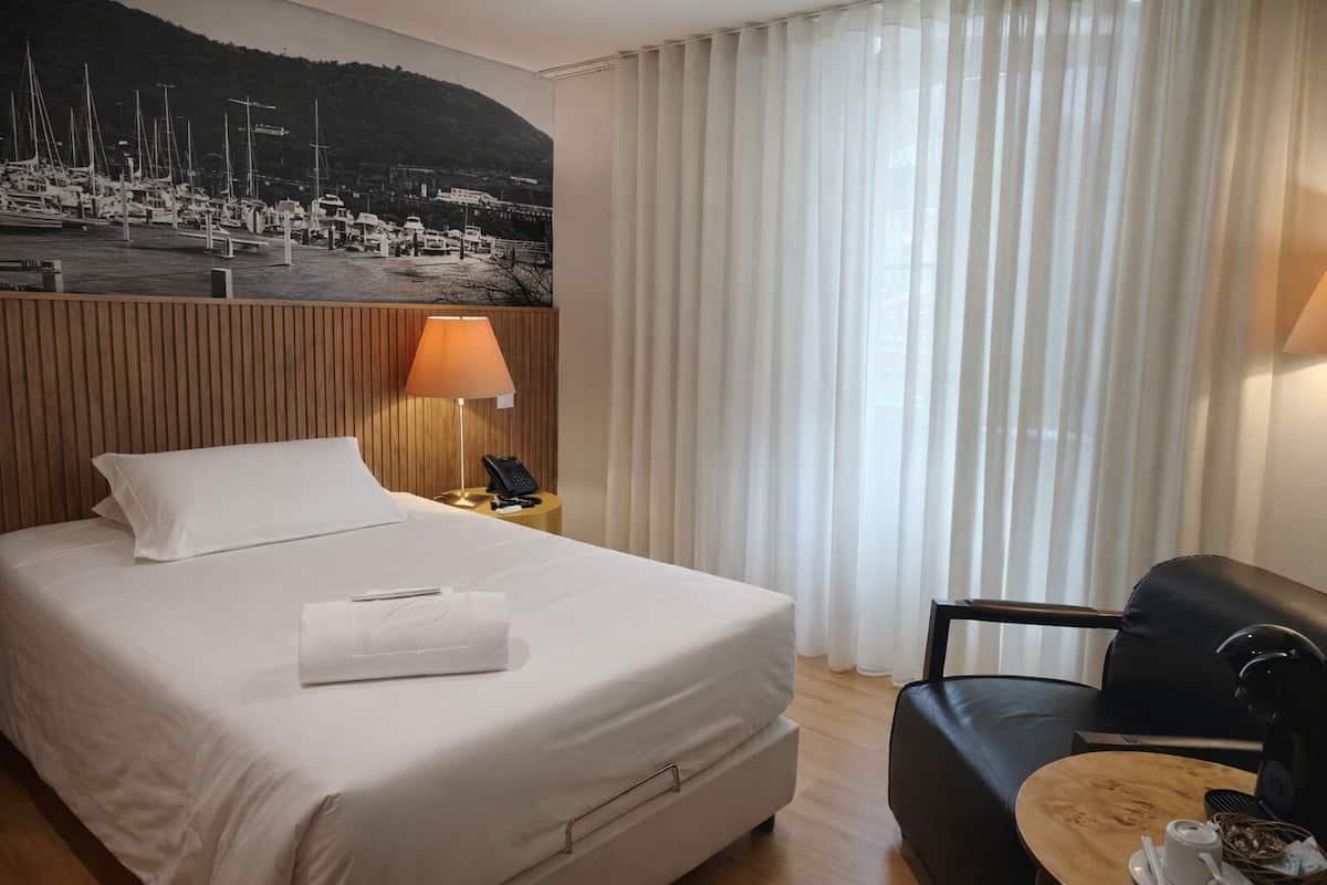 Una habitación de hotel con cama, mesita de noche, lámpara, silla y mesa.